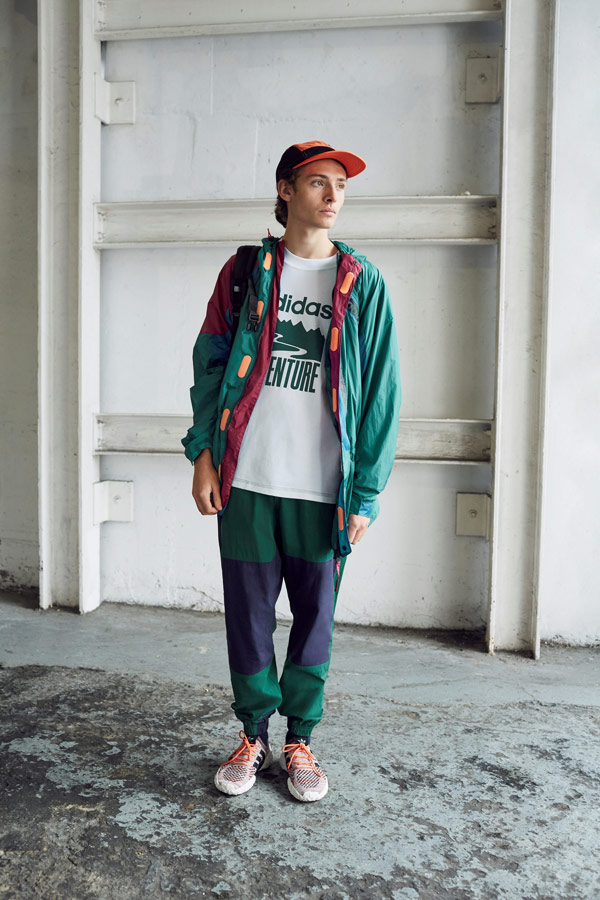 adidas Originals Atric Pack — oblečení — šusťáková zelená bunda s kapucí — bílé tričko s potiskem — modro-zelené šusťákové tepláky — boty F/22 Primeknit — oranžová kšiltovka